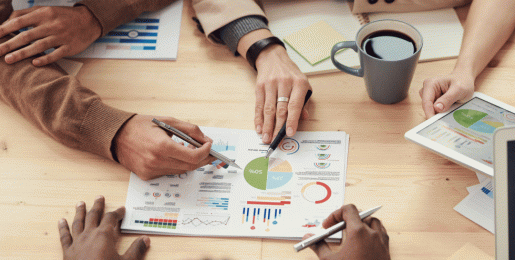 several people holding pens review pages graphs around a table